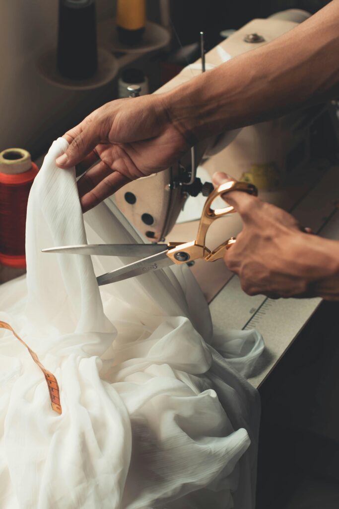 A detailed view of a person using scissors to cut fabric near a sewing machine.
