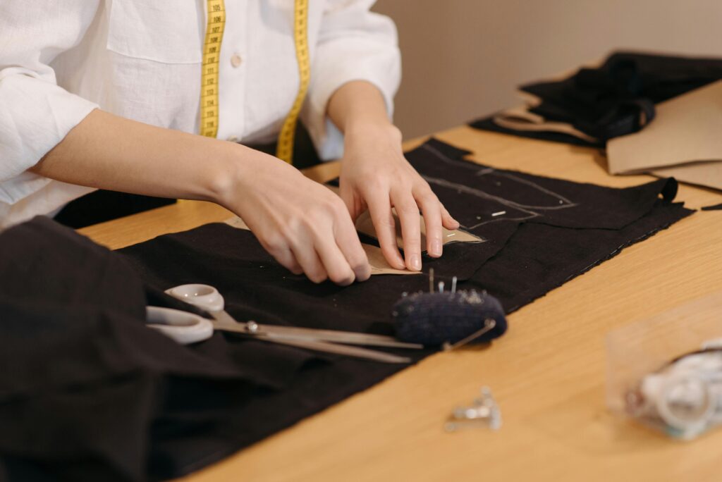 Close-up of a tailor cutting fabric on a workspace with sewing tools.